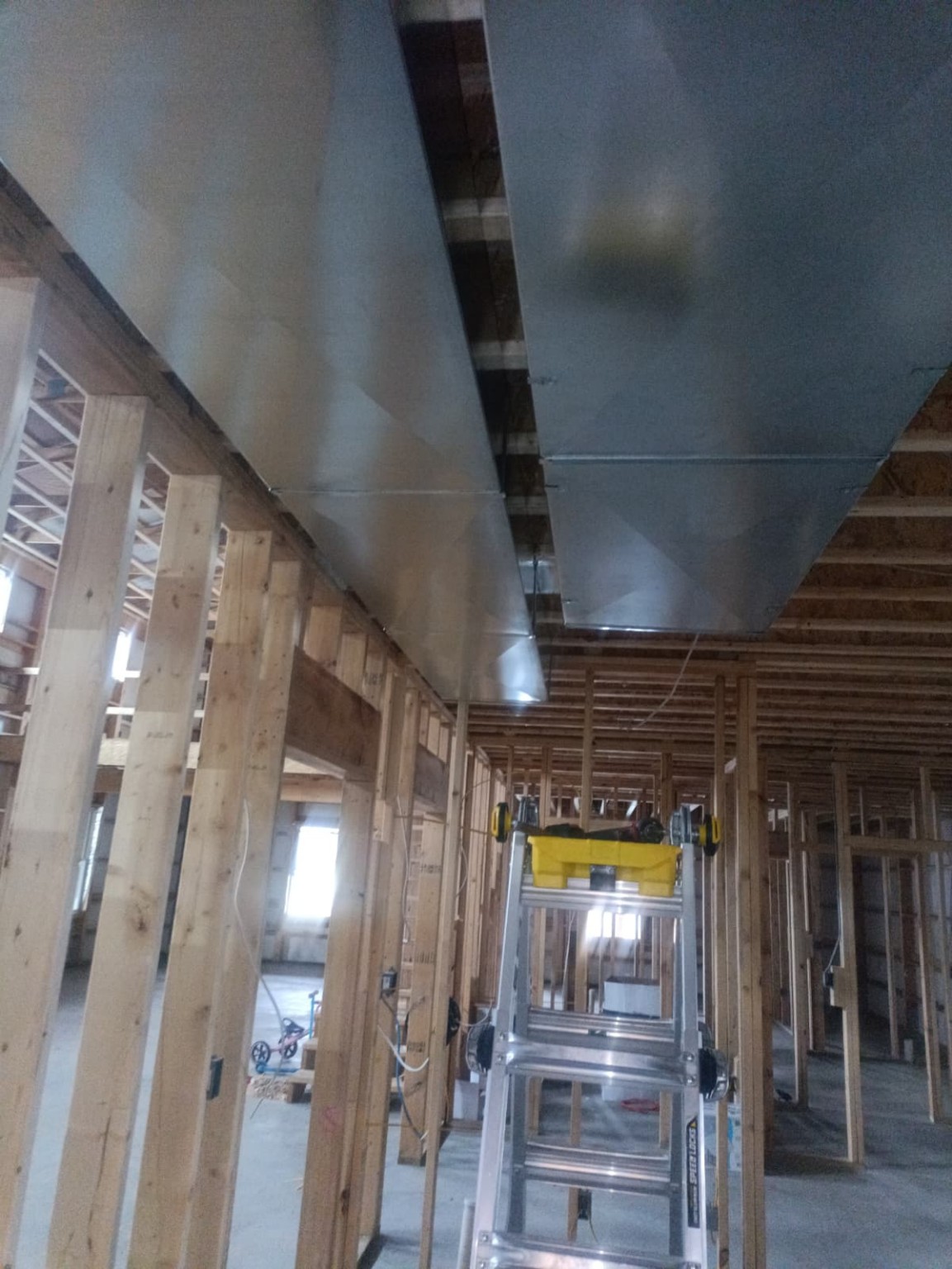 New construction HVAC rough-in with galvanized trunk lines hung on ceiling joists